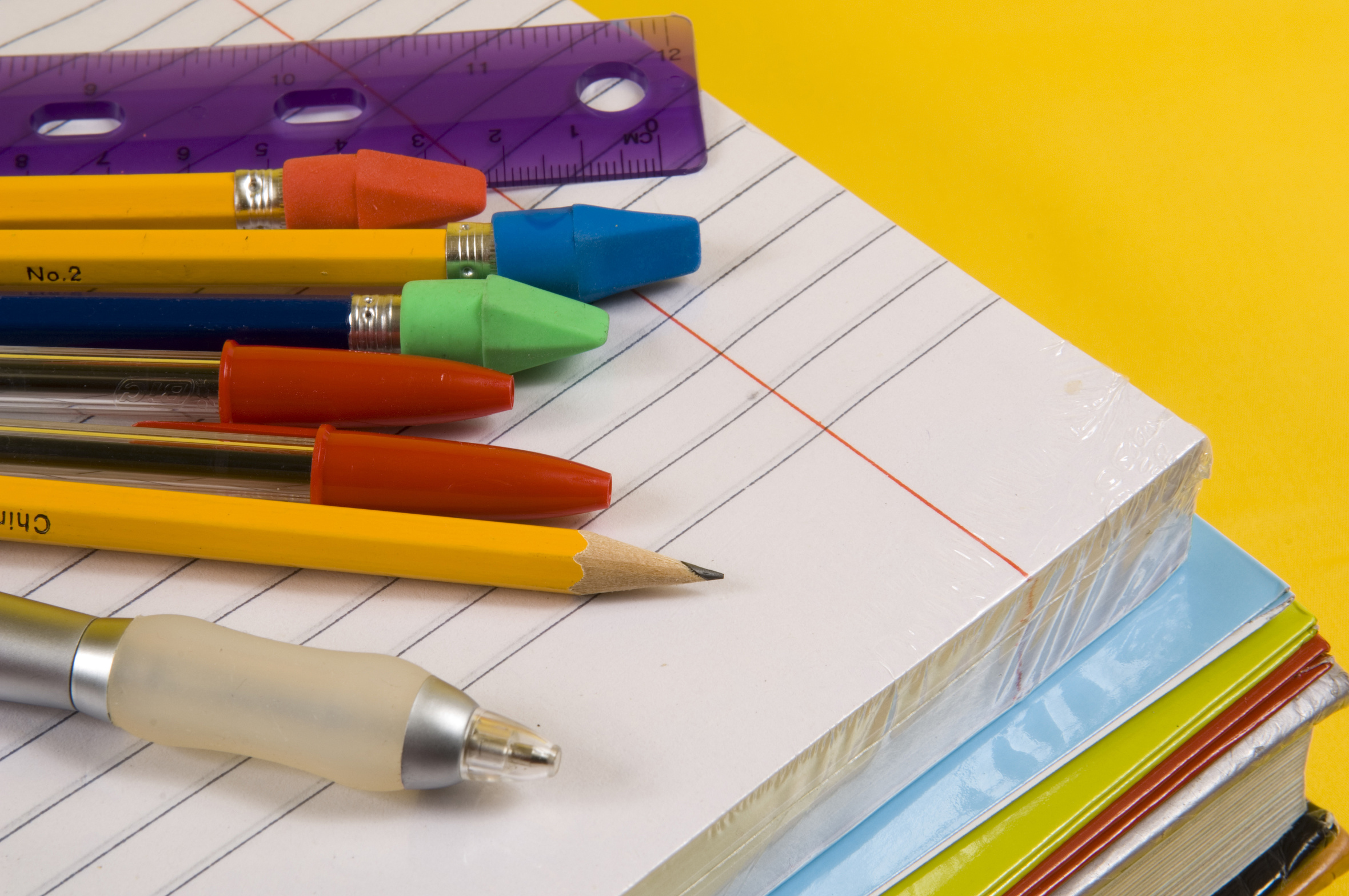 school supplies on yellow background with pen, pencils, rulers, paper and folders